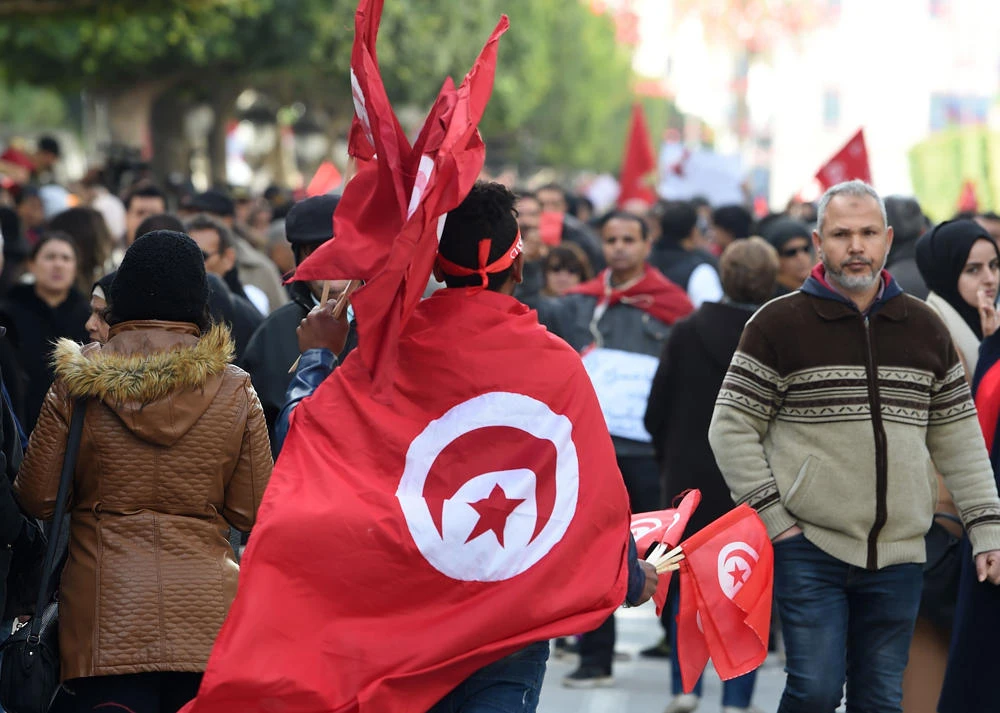 Tunisians wave flags during a rally marking the eighth anniversary of the 2011 revolution in front of the headquarter of the Tunisian General Labour Union in the capital Tunis on January 14, 2019. (AFP / Fethi Belaid)