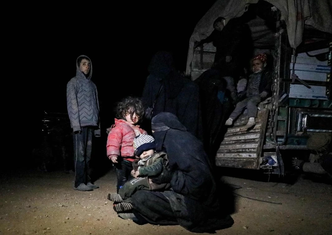 A woman wearing a niqab (full face veil) sits on the ground carrying a child by the back of a truck near the Omar oil field in the countryside of the eastern Syrian Deir Ezzor province on January 25, 2019. (AFP)