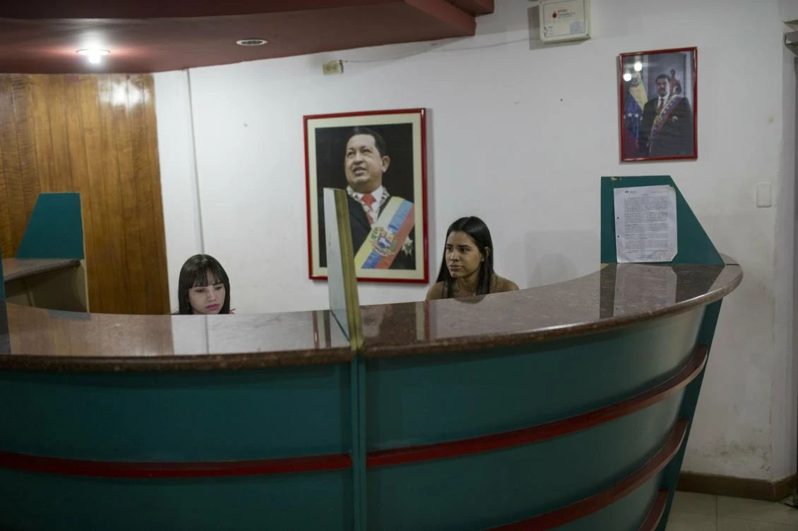 Receptionists work under portraits of Hugo Chavez and Nicolas Maduro. Venezuela is currently in the throes of a political standoff between opposition leader Juan Guaido and Nicolas Maduro. (AP Photo)