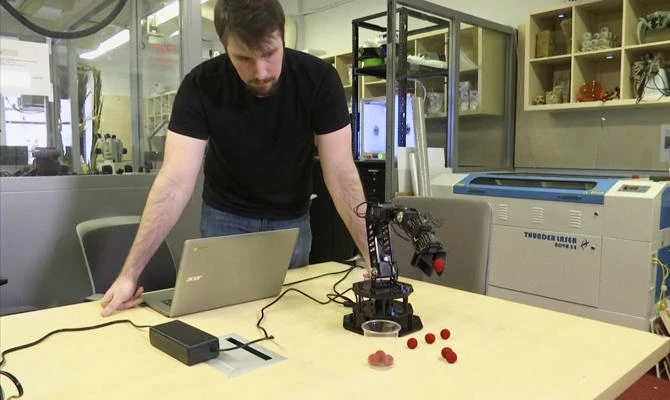 In this image made from a Feb. 1, 2019, video, Robert Kwiatkowski, a graduate student at Columbia University, demonstrates a robotic arm picking up a red ball and dropping it in a cup at the school in New York. (AP Photo)