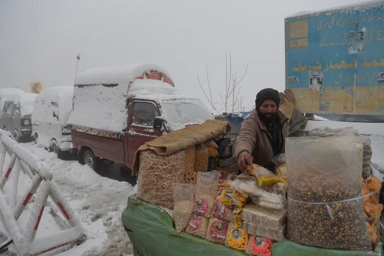 A Pakistani vendor arranges his stall near vehicles covered with snow during a snowfall in Murree, some 65 km north of Islamabad, on January 5, 2019. (File/AFP)