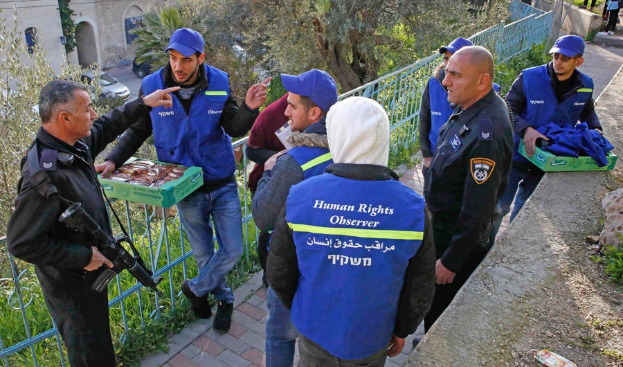 An Israeli policeman (L) talks to volunteers from the Palestinian Youth Against Settlements organization after Israeli soldiers closed the area around al-Shuhada street in the divided West Bank city of Hebron on February 13, 2019. (AFP / HAZEM BADER)