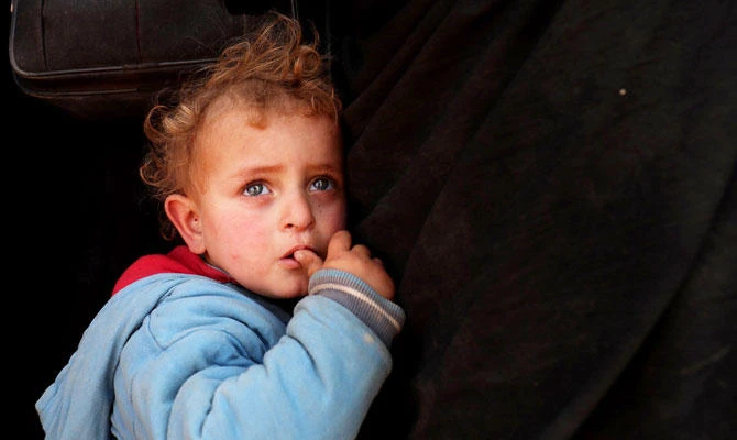 A child stands by his mother as civilians fleeing the Daesh group embattled holdout of Baghouz gather in a field on February 13, 2019 during an operation by the US-backed Syrian Democratic Forces (SDF) to expel the Daesh from the area, in the eastern Syrian province of Deir Ezzor. (AFP)