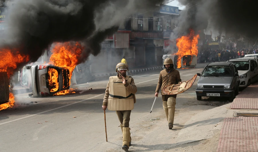 Indian policemen walk past vehicles set on fire in Jammu by a mob during a protest on Feb. 11, 2019 against an attack on a paramilitary convoy the day before. (AP Photo/Channi Anand)