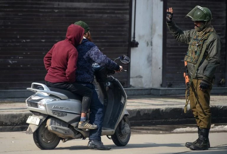 An Indian paramilitary trooper stops Kashmiris driving on a scooter for a security check in Srinagar on February 11, 2019. (AFP)