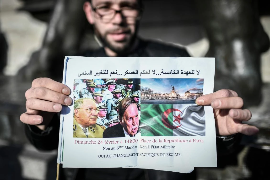 A man holds up a sign that reads, 'No to a 5th mandate, no to a military state, yes to peaceful change', as people gather to protest against Algerian president's bid for a fifth term in office on February 24, 2019 at the Place de la Republique in Paris. (AFP)