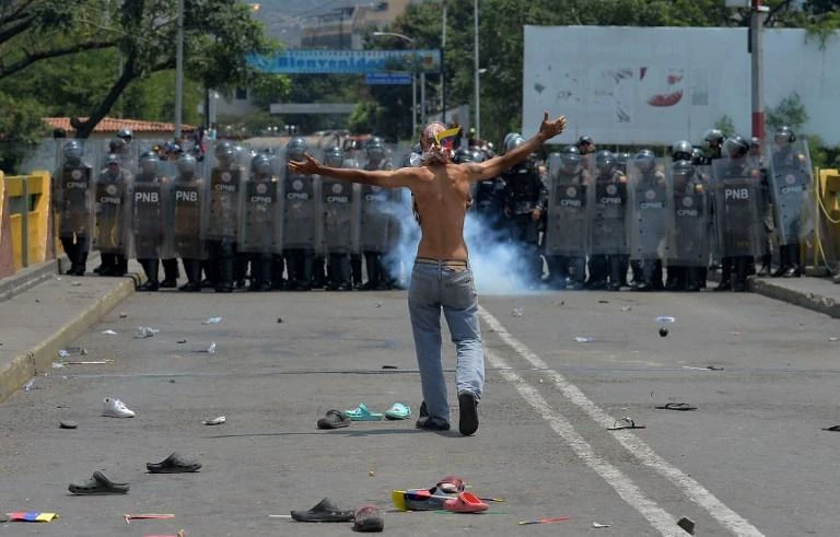 A demonstrator confronts Venezuelan national policemen standing guard at the Simon Bolivar international bridge, which connects to the Colombian border. (AFP)