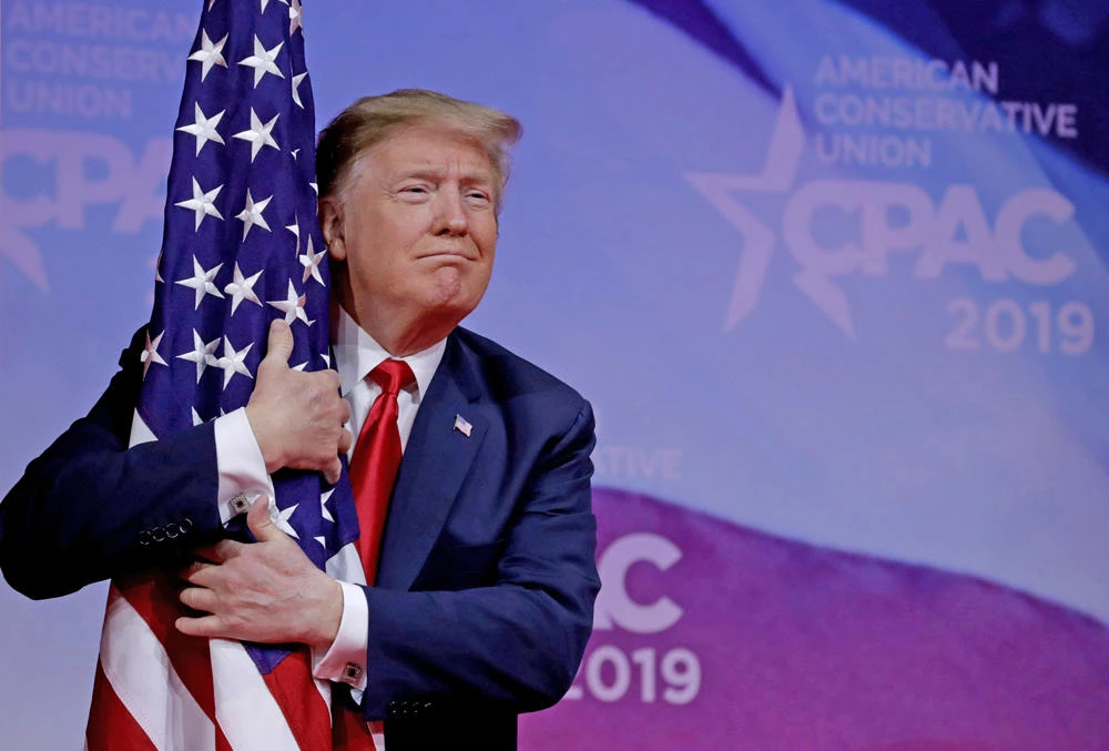 US President Donald Trump hugs American flag at the Conservative Political Action Conference (CPAC) annual meeting at National Harbor near Washington on March 2, 2019. (REUTERS/Yuri Gripas)