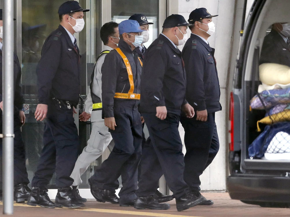 Former Nissan Chairman Carlos Ghosn, in blue cap, walks out with security guards from Tokyo Detention Center in Tokyo. (AP/Eugene Hoshiko)