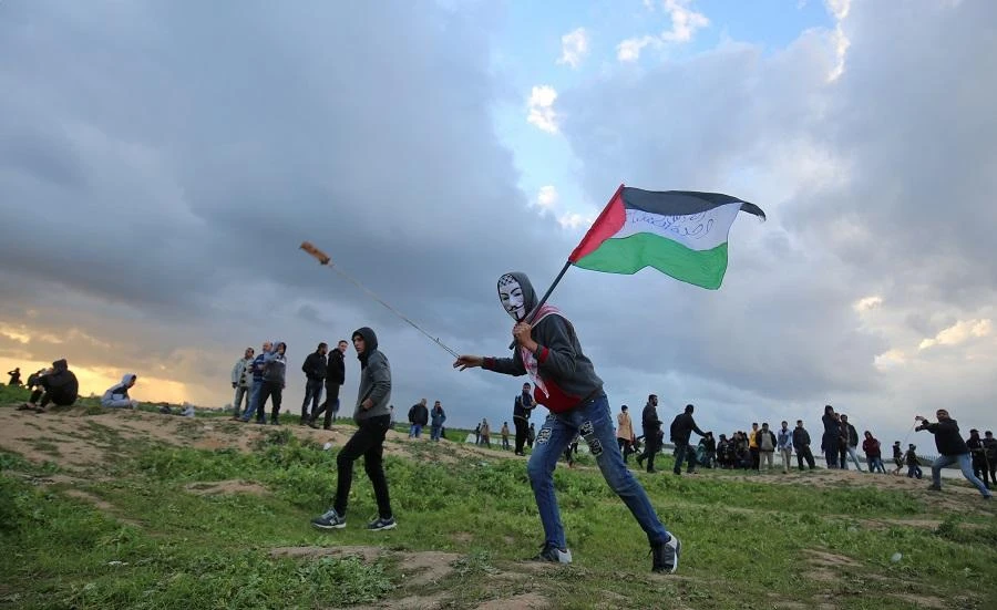 A Palestinian protester wearing a Guy Fawkes mask while holding a Palestinian flag and hurling a slingshot is seen during clashes following a demonstration along the border with Israel east of Gaza City on March 1, 2019. (File/AFP)