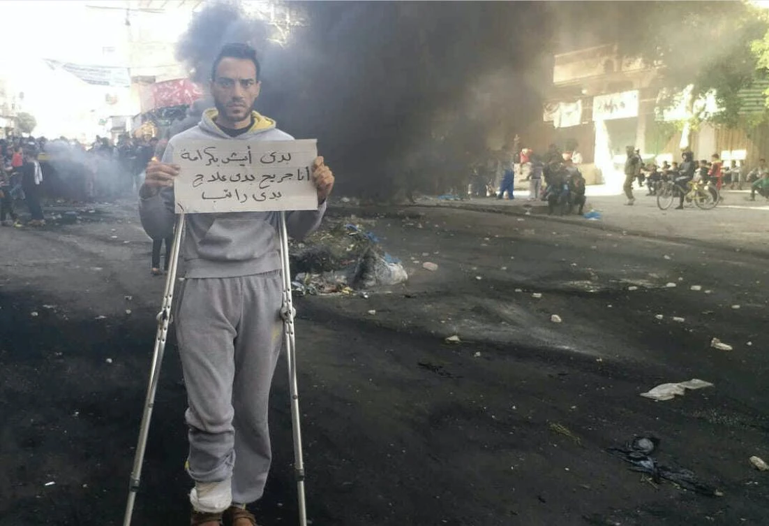 This photo provided by Palestinian journalist Osama al-Kahlout shows a protestor holding a sign that reads in Arabic, "I want to live in dignity; I'm wounded and need treatment and a salary," during a protest in Deir al Balah, central Gaza Strip, on Friday, March 15, 2019. (Osama al-Kahlout via AP)