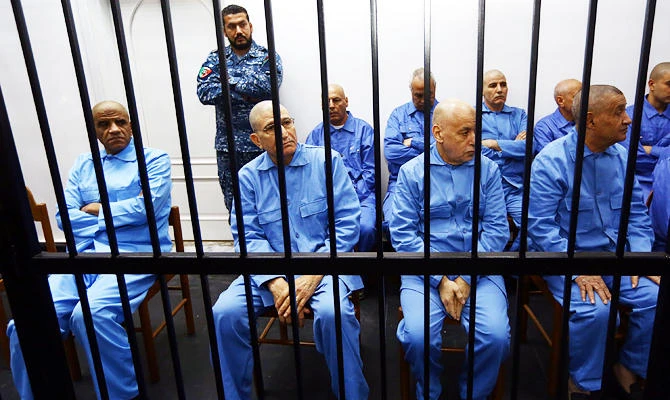 Former Libyan intelligence chief Abdullah al-Senussi (L), dressed in prison blues, sits along with other defendants behind the bars of the accused cell during a hearing as part of his trial in a courthouse in Tripoli on December 28, 2014. (AFP)