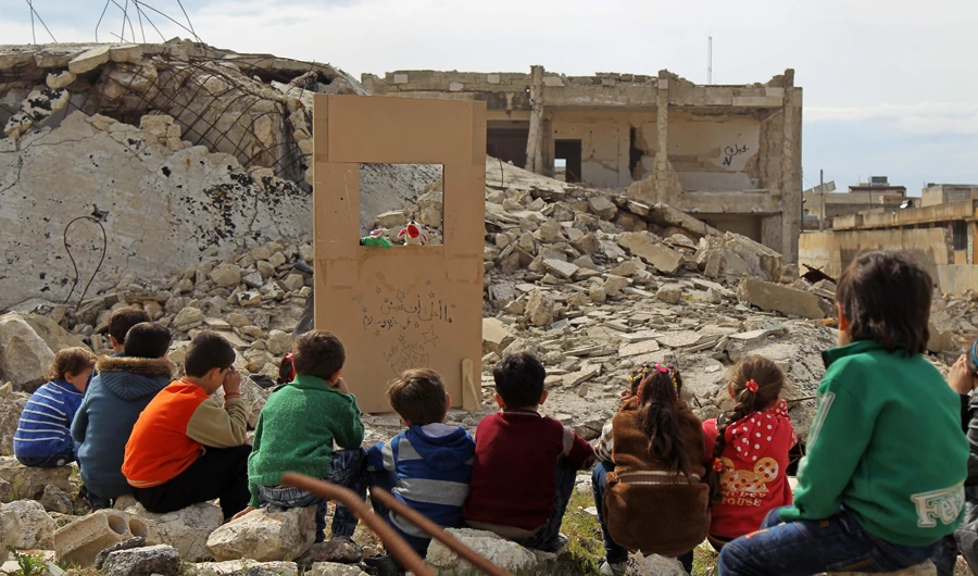 Children watch a puppet show performed by a Syrian actor, through a makeshift puppet theatre set up among the rubble of collapsed buildings in the town of Saraqib in the rebel-held northern Idlib province. (AFP)