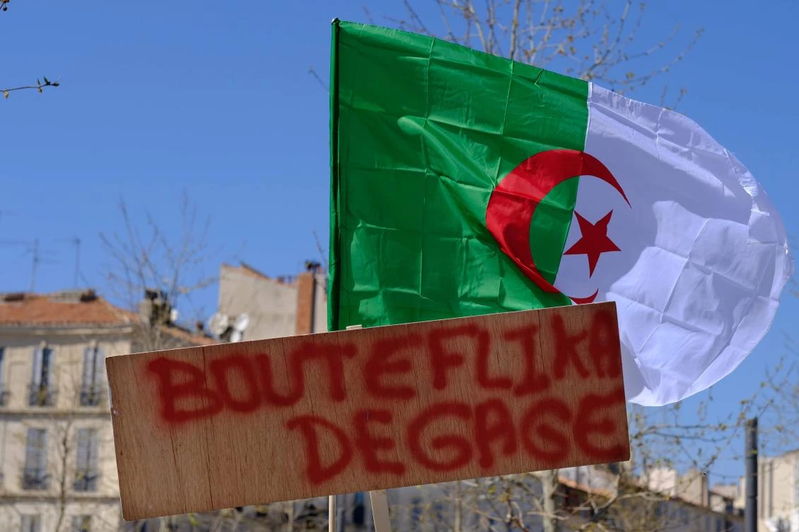 An Algerian flag is seen behind a placard reading "Bouteflika, bugger off" during a rally to demand an end to President Bouteflika's rule on March 31, 2019 in Marseille. (AFP)