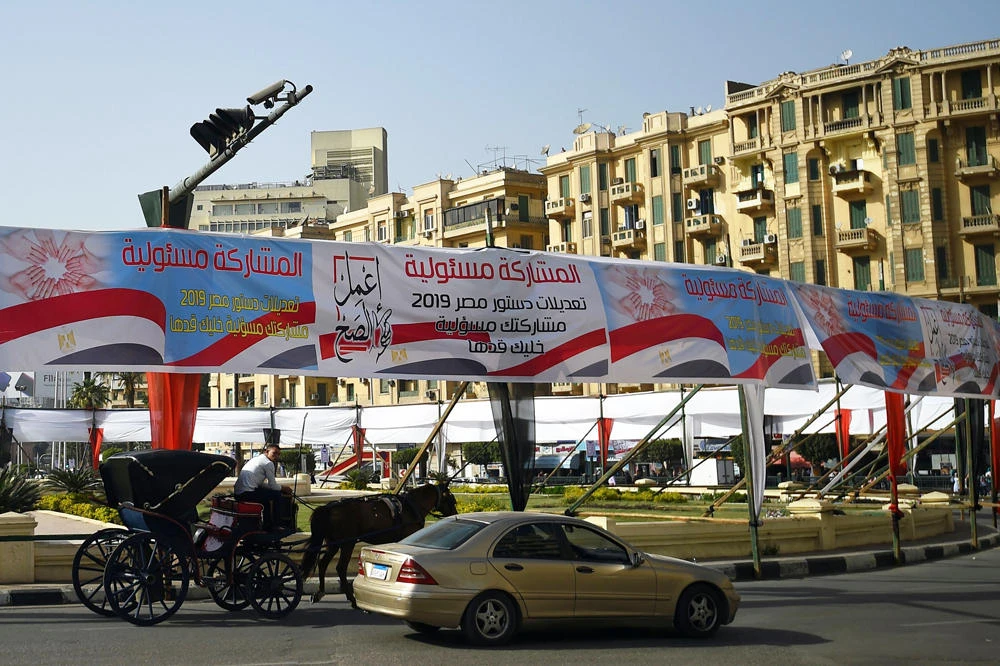Egyptians pass under banners in Cairo reading in Arabic "Do what is right", and "Participation is your responsibility", urging voters to participate in the upcoming referendum for the constitutional amendments. (AFP / Mohamed el-Shahed)