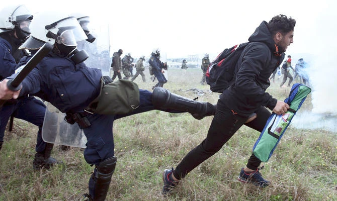 A police officer kicks a protesting migrant during clashes outside a refugee camp in the village of Diavata, west of Thessaloniki, northern Greece, Saturday, April 6, 2019. (AP)