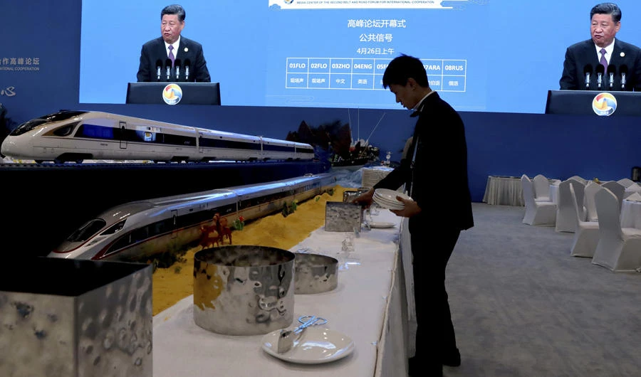 A waiter prepares for lunch next to model high speed trains and screens live broadcasting Chinese President Xi Jinping opening the Second Belt and Road Forum in Beijing Friday, April 26, 2019. (AP Photo/Ng Han Guan)