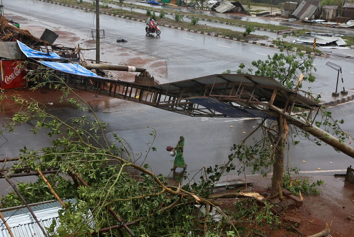 A woman carries pitchers next to uprooted trees and a fallen signboard following Cyclone Fani in Khordha district in the eastern state of Odisha, India, May 3, 2019. (Reuters)