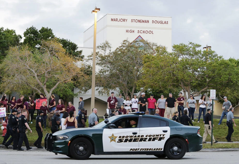 In this Feb. 28, 2018 file photo, a police car drives near Marjory Stoneman Douglas High School in Parkland, Florida, as students return to class for the first time since a former student opened fire there with an assault weapon. Florida Gov. Ron DeSantis has signed a bill that will allow more classroom teachers to carry guns in school, a response to last year's mass shooting at a Parkland high school. (AP Photo/Terry Renna, File)