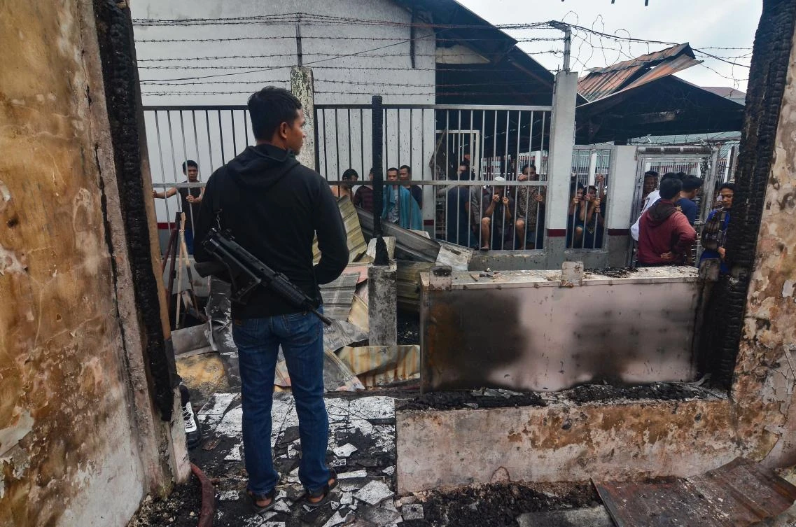 An armed plainclothes policeman (L) secures the around around Siak prison in Siak Sri Indrapura in Riau province on May 11, 2019 after rioting and a fire broke out at the detention centre leading to a prison break. (AFP)