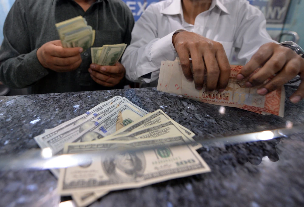 Money dealers counts Pakistani rupees (R) and US dollars at a currency exchange in Islamabad