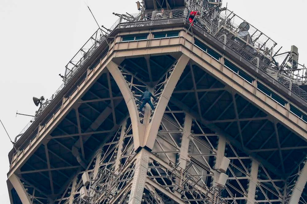 A man (C) climbs up the Eiffel Tower, in Paris, without any protection as a firefighter (R) looks down at him from the top, on May 20, 2019. (AFP)