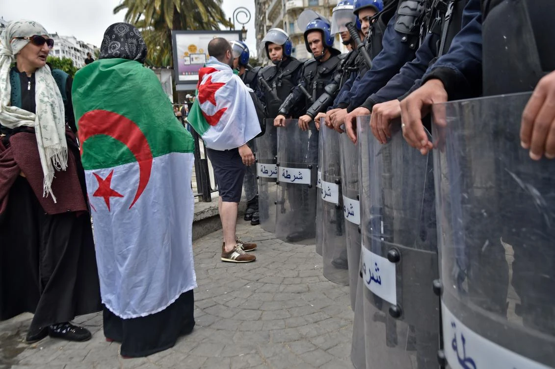 Algerian demonstrators, draped in national flags, stand in front of security forces during an anti-government demonstration in the capital Algiers on May 24, 2019. (AFP)