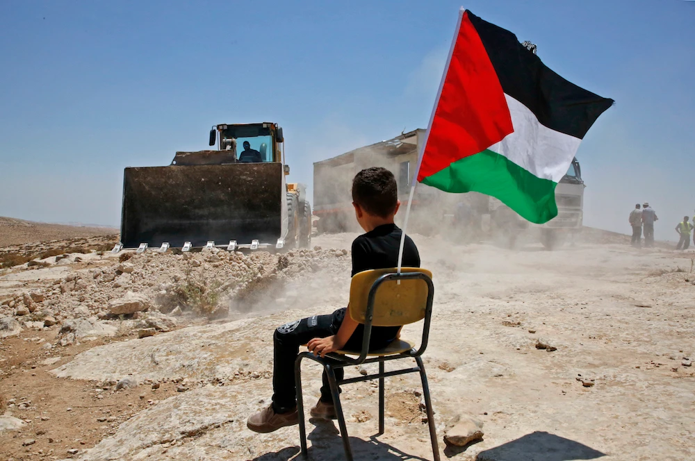 A Palestinian boy sits on a chair with a national flag as Israeli authorities demolish a school site in the village of Yatta, south of the West Bank city of Hebron. (File/AFP)