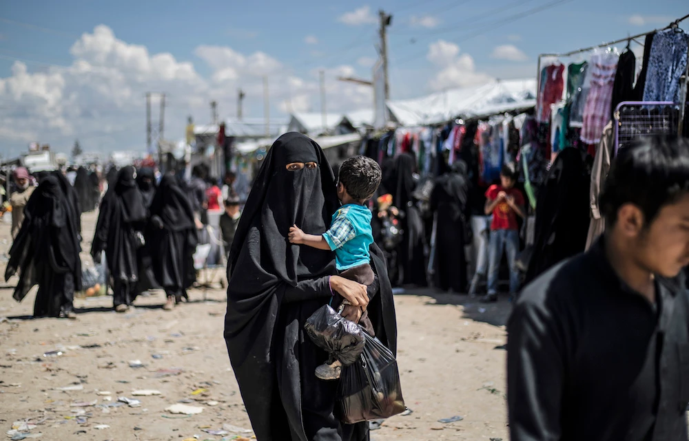 A woman displaced from Syria’s eastern Deir Ezzor province, carries child as she walks in Al-Hol camp for displaced people, in Al-Hasakah governorate in northeastern Syria. (File/AFP)