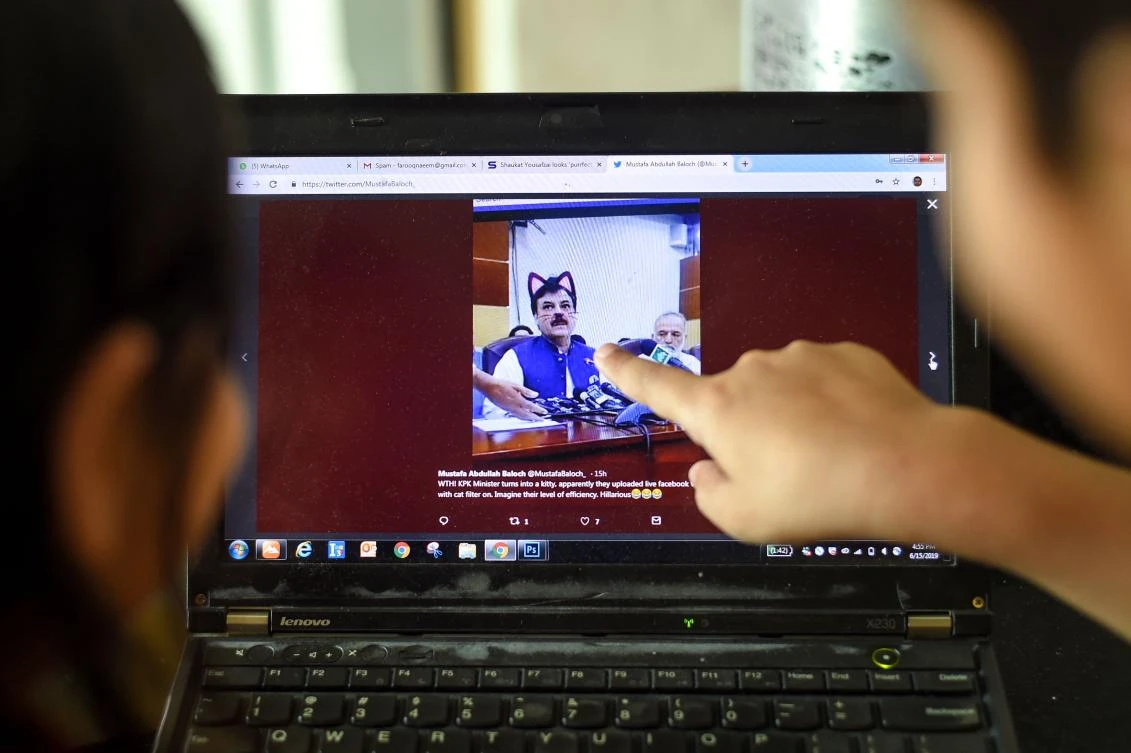 Pakistani children point at a computer screen showing a screen grab of a press conference attended by provincial minister Shaukat Yousafzai and streamed live on social media, with his talk going live with a cat filter. (AFP)