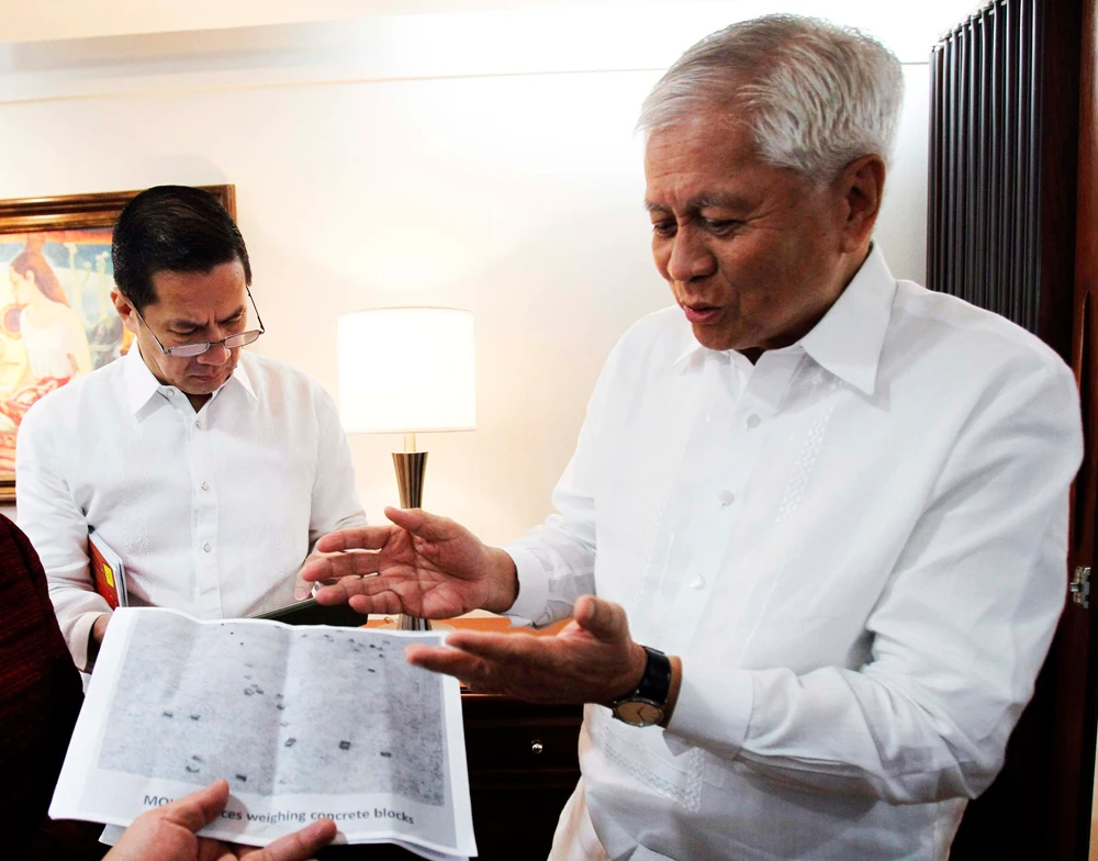 In this September 4, 2013 photo, then Philippine Foreign Affairs Secretary Albert Del Rosario shows an aerial handout photograph of concrete blocks from China on the disputed Scarborough Shoal in the South China Sea. (REUTERS file photo)