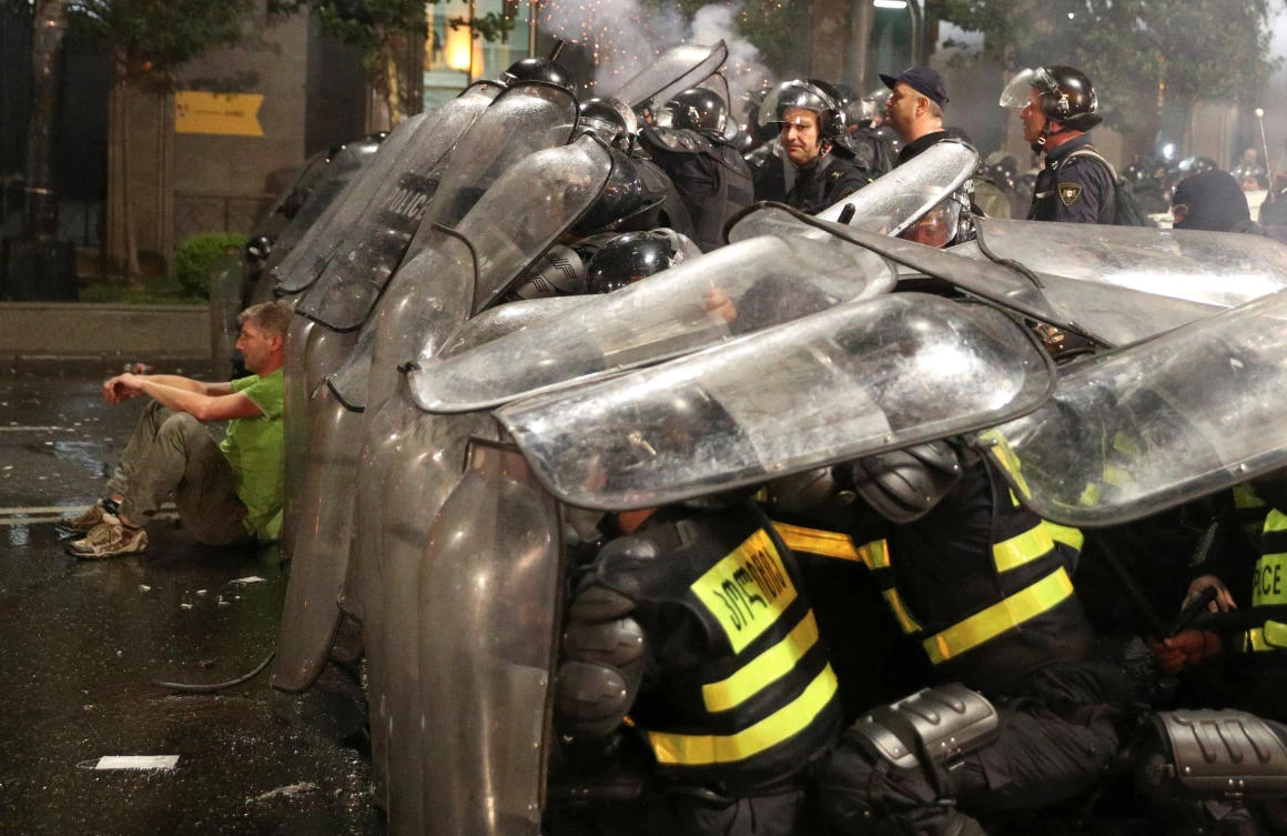 A protester sits on the ground next to riot policemen, who cover themselves with shields during a rally against a Russian lawmaker’s visit in Tbilisi, Georgia. (Reuters)