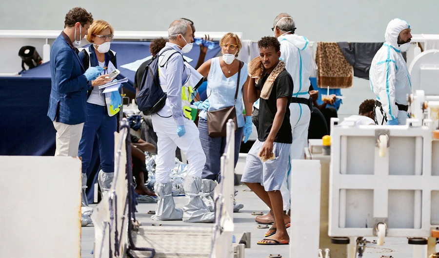 Officials wear masks and protective suits as they stand with migrants on the deck of the Italian Coast Guard vessel "Diciotti" in the Sicilian port of Catania, on August 23, 2018, as they wait to disembark following a rescue operation at sea. (AFP)
