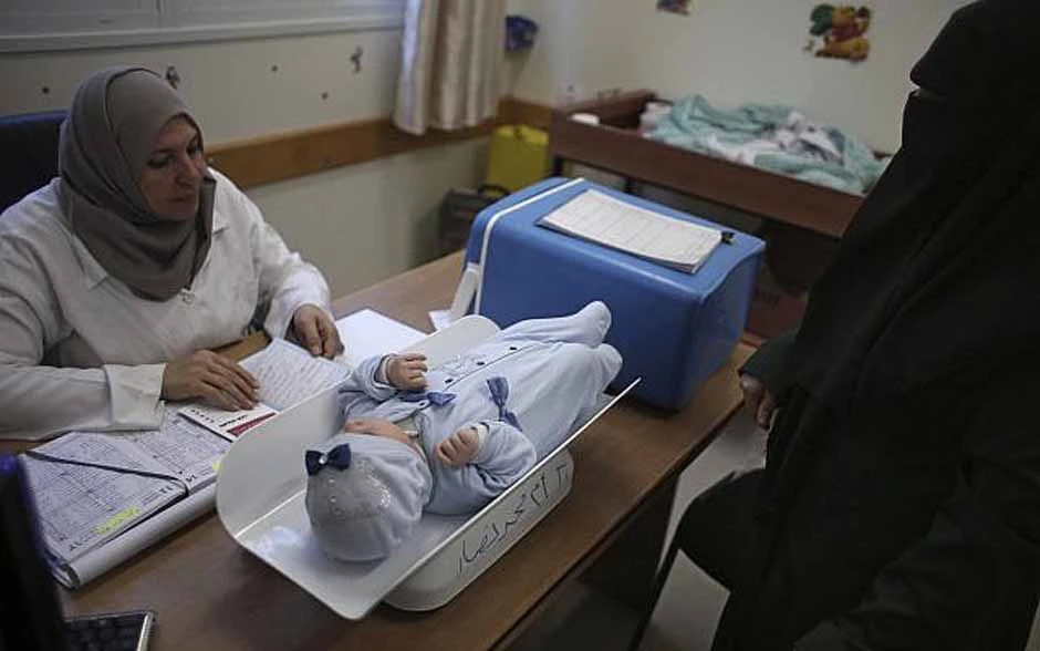 A Palestinian woman has her child checked at an UNRWA-run clinic in the Shati refugee camp, Gaza City. (AP Photo)