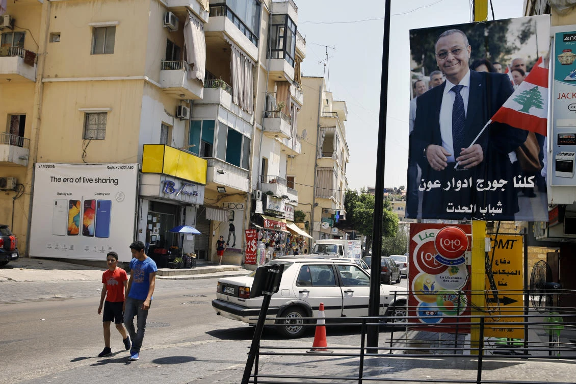 In this Monday, June 24, 2019 photo, a poster shows George Aoun, head of the municipality of the village of Hadat, with Arabic that reads "We are all George Edward Aoun. (AP)