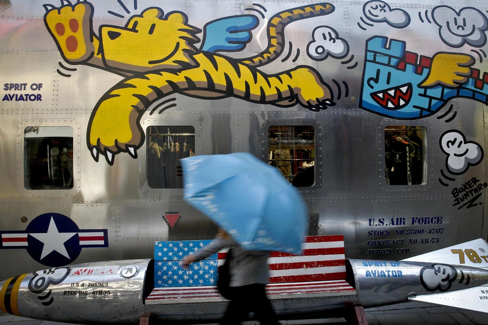 In this May 13, 2019, file photo, a woman walks by a bench painted with an American flag outside a fashion boutique selling US brand clothing at the capital city's popular shopping mall in Beijing. (AP Photo/Andy Wong, File)
