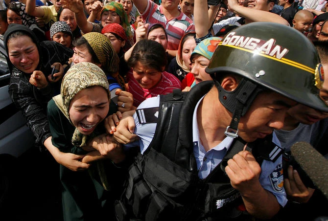 A woman holds onto a Chinese policeman as a crowd of locals confront security forces along a street in the city of Urumqi, in China's Xinjiang Autonomous Region on July 7, 2009. (REUTERS/David Gray/File Photo)