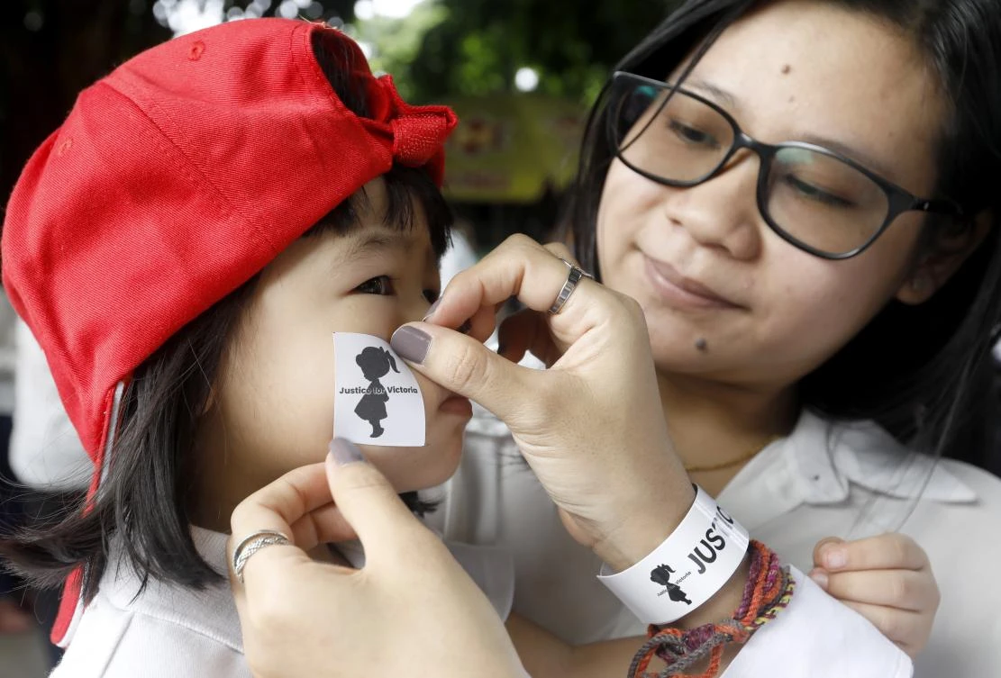 A woman puts sticker on the cheek of young girl during a protest calling for justice in a rape case in Yangon, Myanmar on Saturday, July 6, 2019. (EPA)