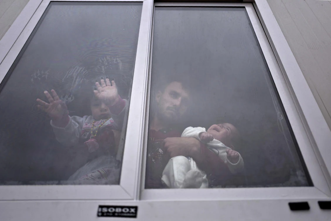 Refugee Siban Assad, 20, from Al-Hasaka, Syria, looks out from the window of his shelter while holding his daughters, Ruba, one month, and Maldar, 1, at the Ritsona , Greece, refugee camp, about 86 kilometers (53 miles) north of Athens. (File/AP/Muhammed Muheisen)