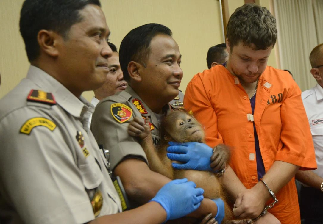 Russian tourist Andrei Zhestkov, right, stands near a police officer in this March 25, 2019 photo after he was arrested after attempting to smuggle a drugged orangutan out of Indonesia. (AFP)