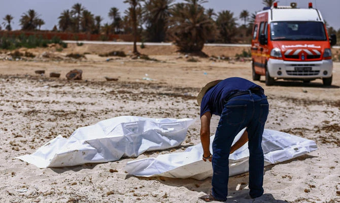 A representative of the Tunisian Red Crescent association checks bodies recovered from a boat carrying 86 migrants that capsized off the Tunisian coast while crossing the Mediterranean from Libya to Italy, as they lie on a beach in Aghir in Tunisia's southern island of Djerba on July 6, 2019. (AFP / ANIS MILI)