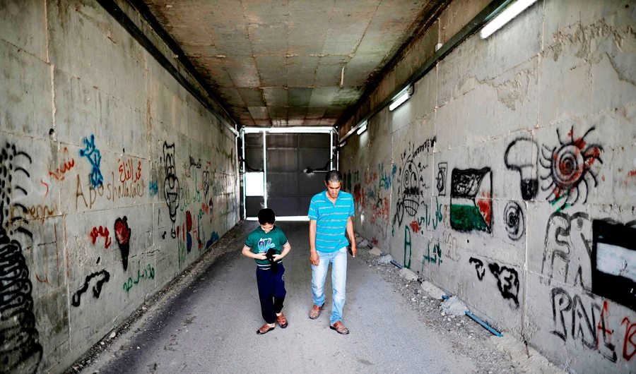 Palestinian Omar Hajajla walks with his son through the tunnel connecting their home in Jerusalem to al-Walajah, their village in the occupied West Bank, on May 30, 2019. (AFP)