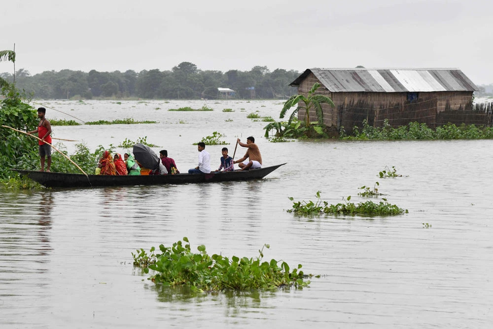 Indian villagers travel by boat through floodwaters near a partially submerged house in Balimukh village of Morigoan district in India's northeastern state of Assam on July 11, 2019. (AFP / Biju Boro)