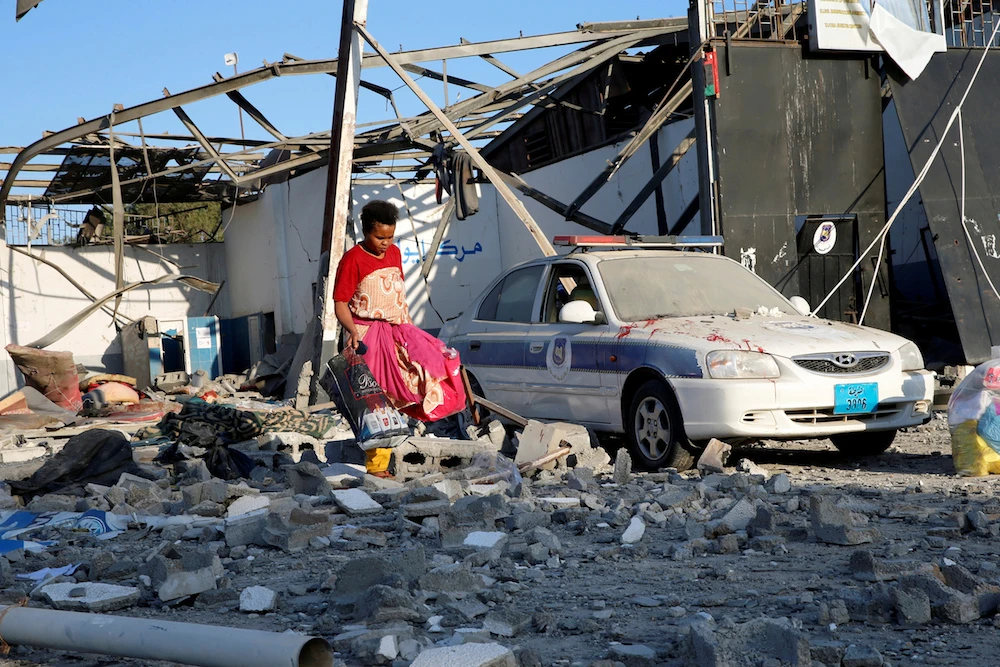 A migrant picks up clothes from among rubble at a detention centre for mainly African migrants that was hit by an airstrike in the Tajoura suburb of the Libyan capital of Tripoli. (Reuters)