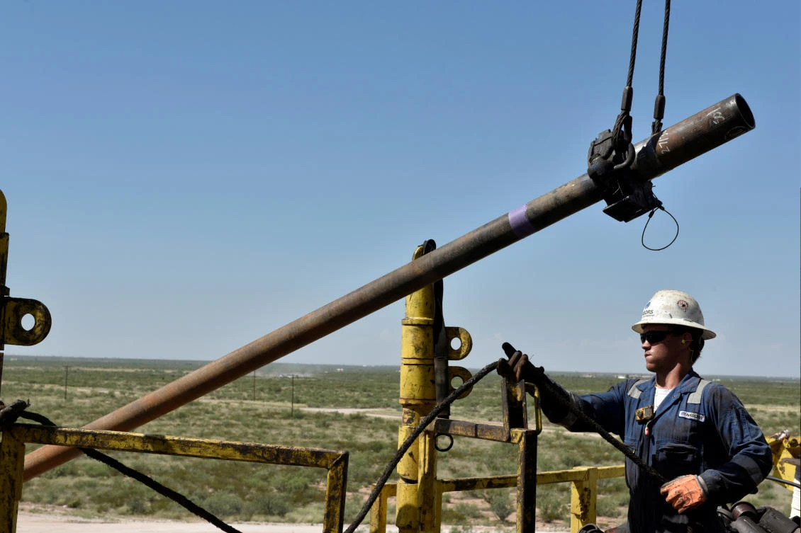 US crude inventories fell 3.1 million barrels, the Energy Information Administration said. Above, a crew member raises a pipe onto the drilling rig floor of an oil rig in the Permian Basin near Wink, Texas. (Reuters)