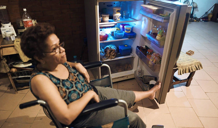 A resident, who remains in a wheelchair due to a broken leg, shows groceries and vegetables in her fridge, in Petare slum, Caracas on July 25, 2019. (AFP)