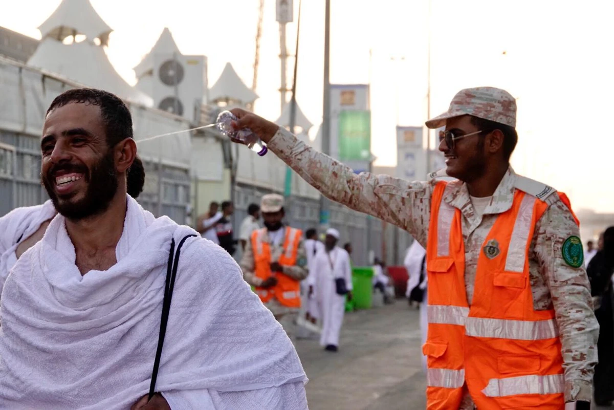 A police officer sprinkles water over the heads of oncoming pilgrims to offer some slight respite from the heat.  (AN photo/Huda Bashatah)