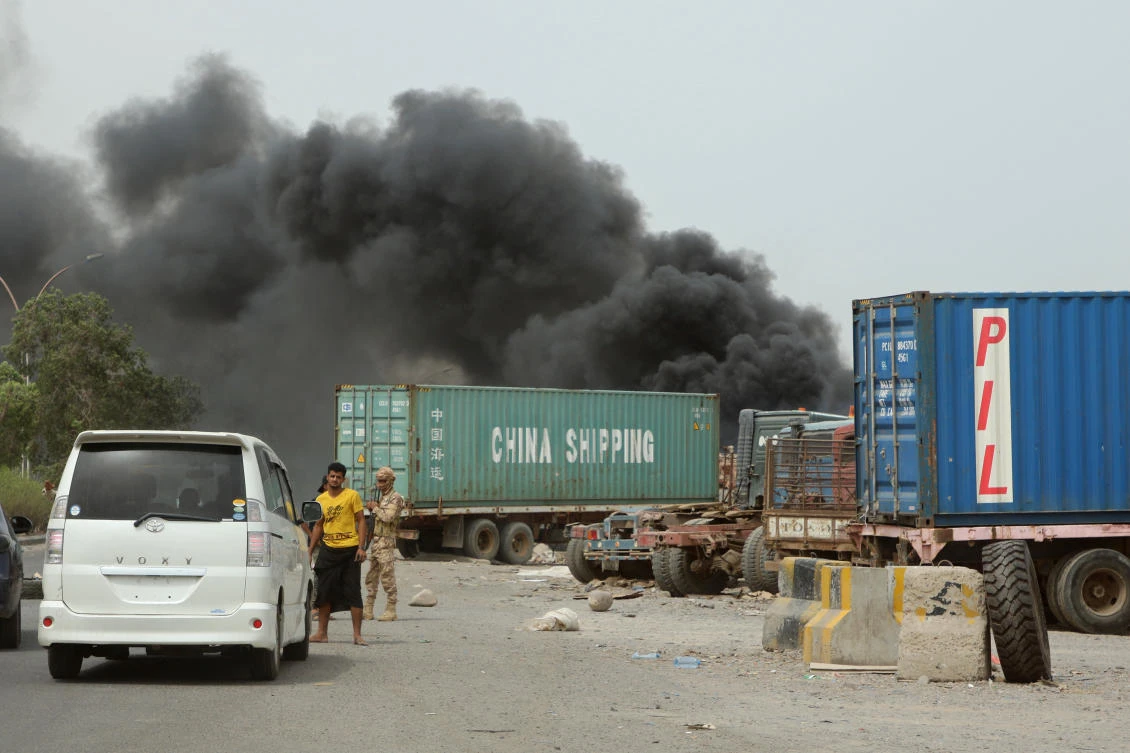 Southern separatists stop cars on a street as smoke billows from a car service shop during clashes in AdenFriday. (Reuters)