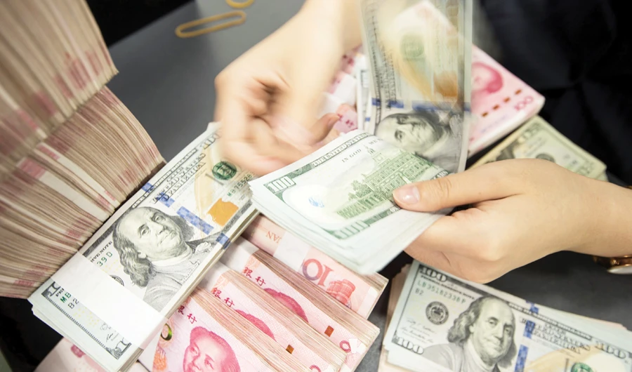 A Chinese bank employee counts 100-yuan notes and US dollar bills at a bank counter in Nantong in China’s eastern Jiangsu province. (AFP)