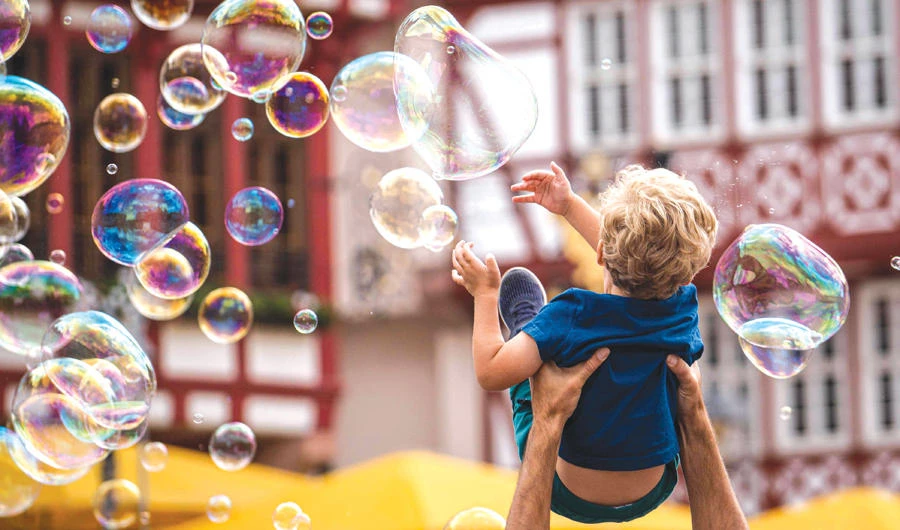 A man lifts a boy for him to reach soap bubbles made by a street artist in Frankfurt. The US-China trade row has a major impact on German exports. (AFP)